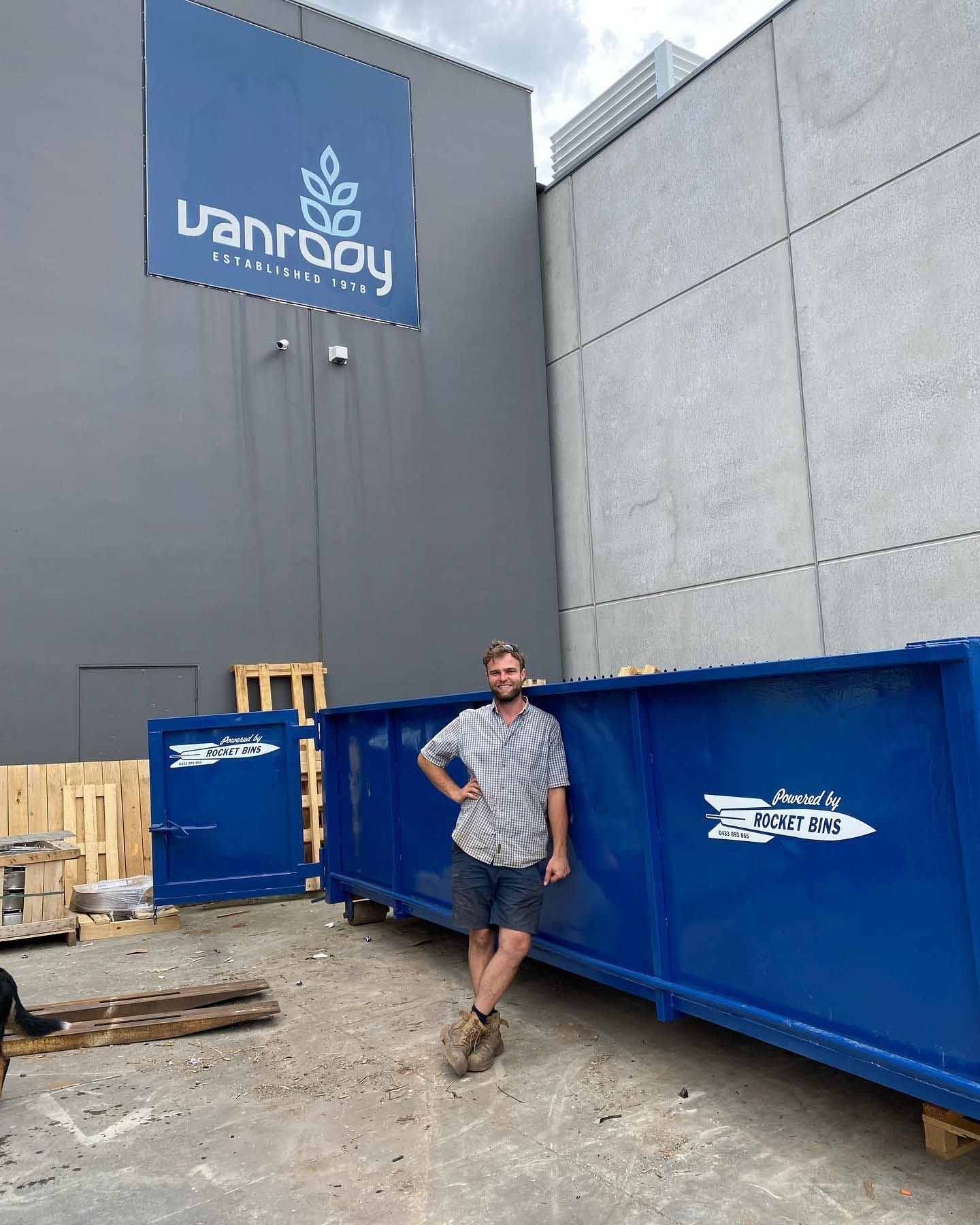 Man standing beside a long blue walk-in bin with its door open outside a commercial building